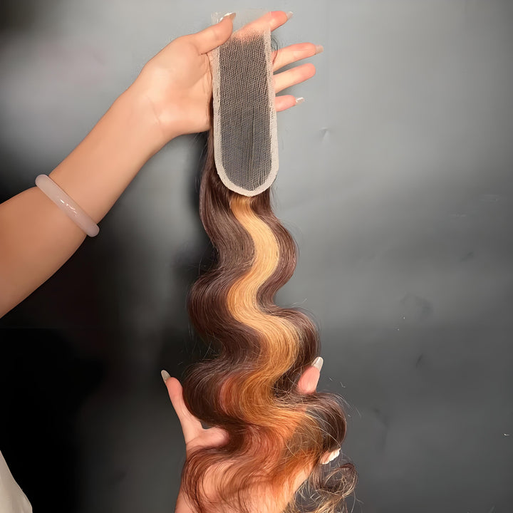 Hand holding a 2×6 body wave lace closure in medium brown with honey blonde highlights, showing lace top and natural wave texture.