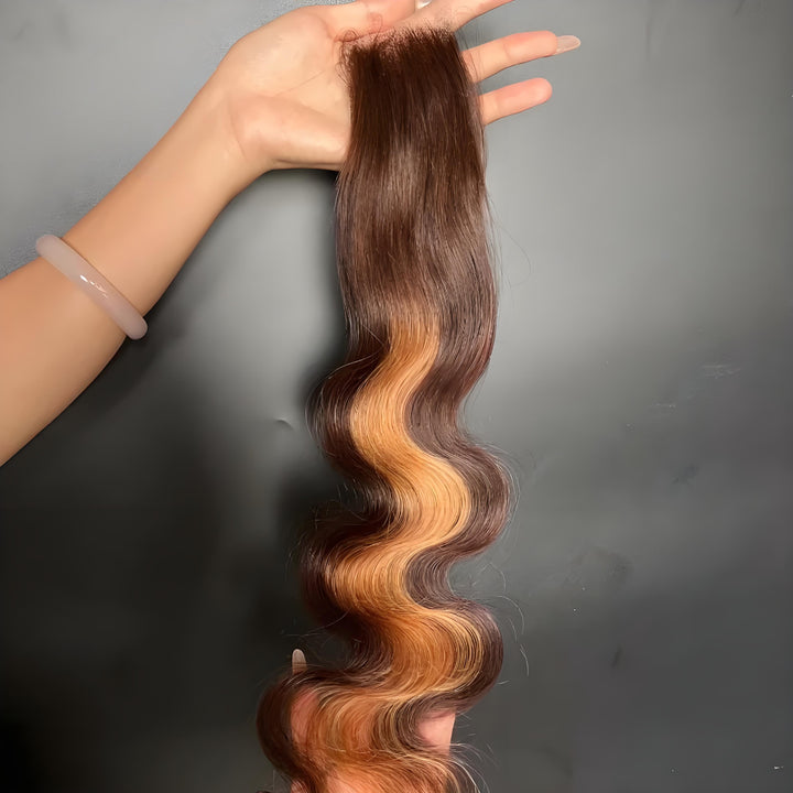 Backside view of 2×6 body wave lace closure in medium brown with honey blonde highlights, hand-held to show smooth root and wave flow.