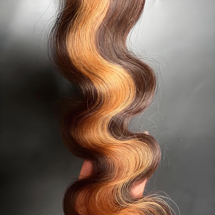 Close-up of a single strand of 2×6 body wave lace closure in medium brown with honey blonde highlights, showing wave pattern and color contrast.
