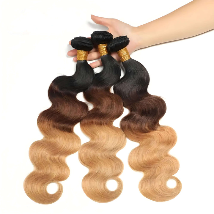 Three body wave bundles in T1B/4/27 ombre displayed in hand, featuring shiny waves and smooth transition from dark to blonde.