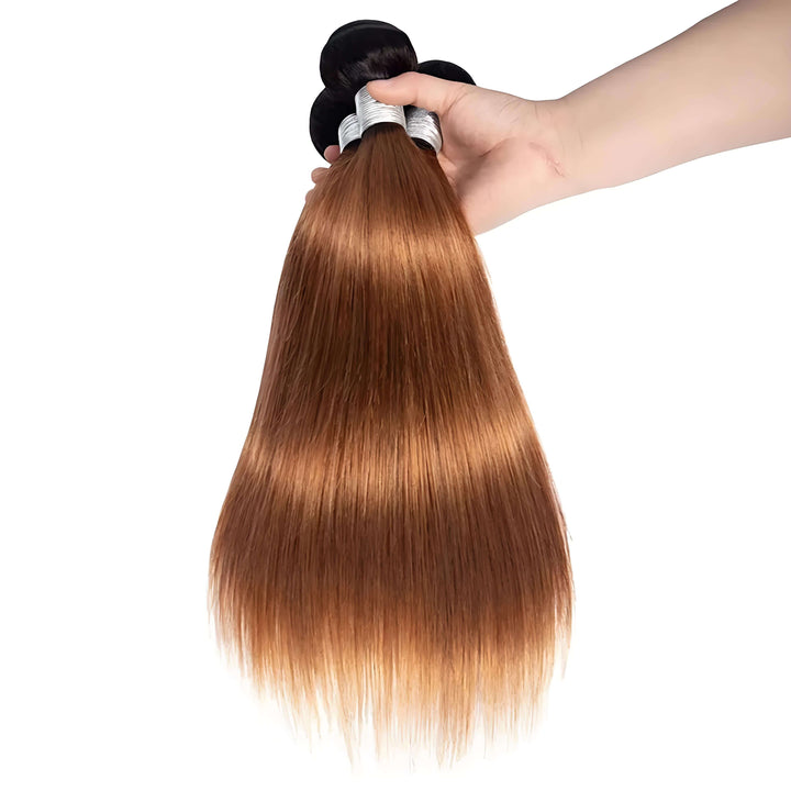 Hand holding straight hair bundles in T1B/30 ombre color, showing smooth transition from off black roots to medium auburn ends.