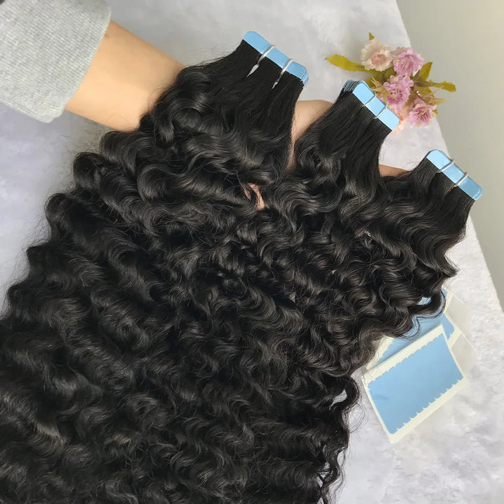 Stacked bundles of natural color water wave tape in hair extensions showing curl consistency and shine.